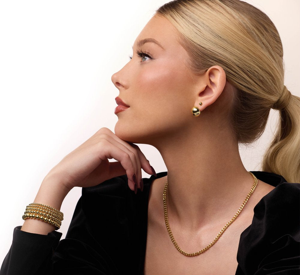 Woman wearing gold jewelry including earrings and a necklace on a plain background