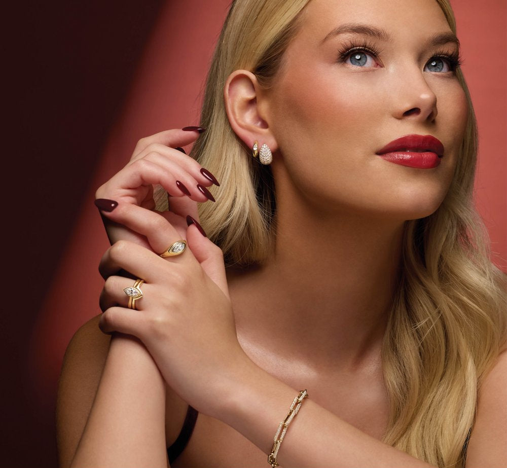 Woman wearing 14K yellow gold round diamond earrings with a red background