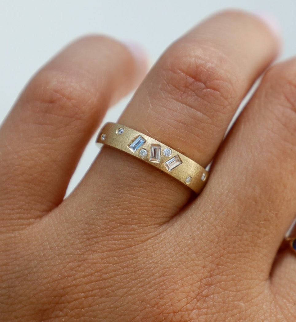Gold ring with gemstones on a finger against a white background