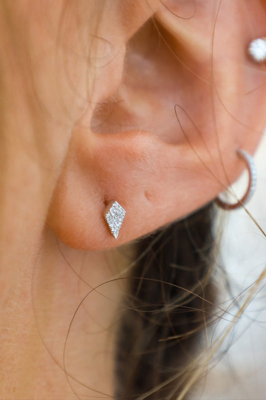 Close-up of an ear wearing a diamond-shaped earring with a blurred background