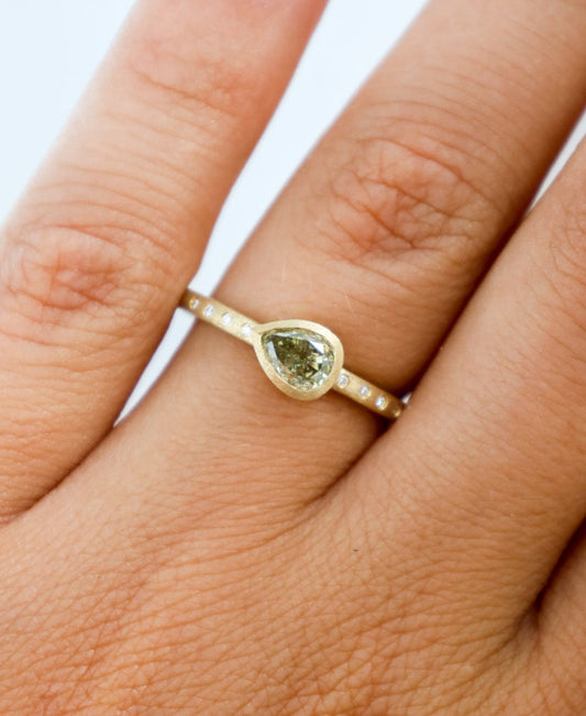 Gold ring with a green gemstone on a person's finger against a white background