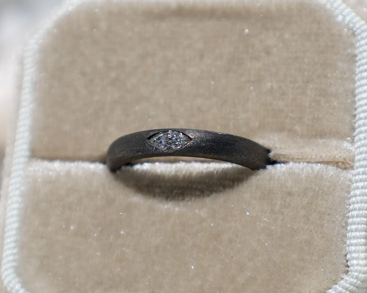 A black gold marquise diamond ring displayed in a ring box, with a visible clear and slightly tinted diamond.