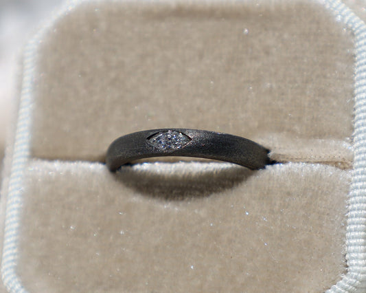 A black gold marquise diamond ring displayed in a ring box, with a visible clear and slightly tinted diamond.