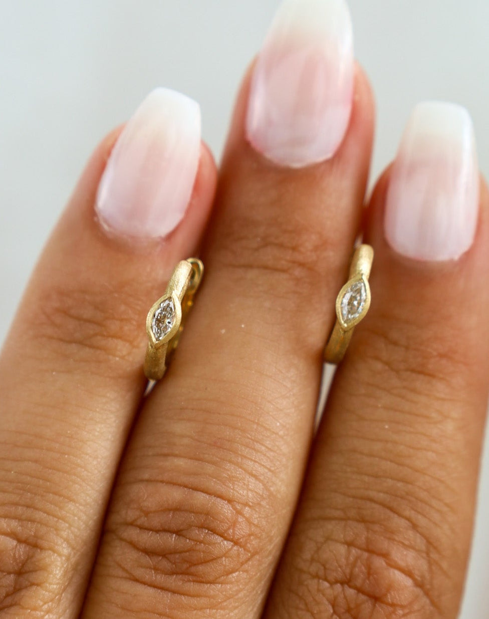 Gold ring with a diamond on a finger against a neutral background