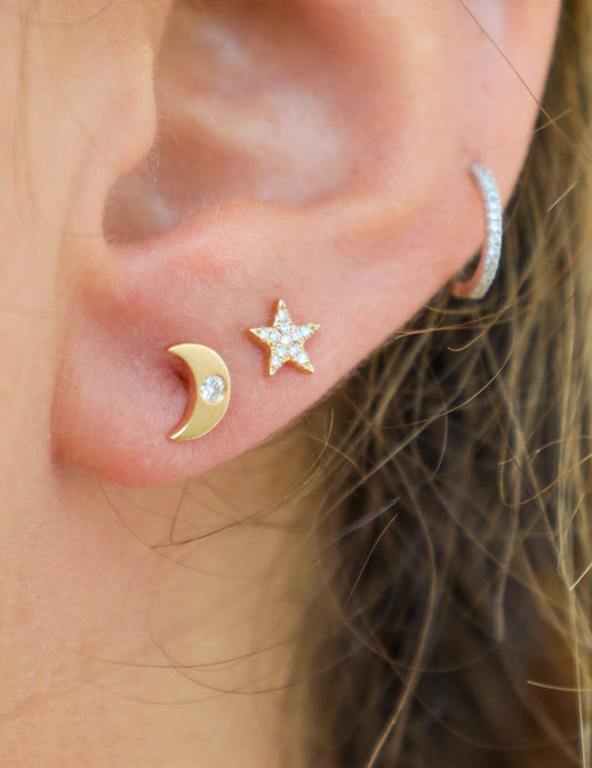 Close-up of an ear wearing gold earrings with a star and crescent moon design.