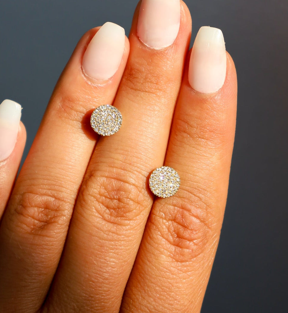 A hand holding a gold diamond disc earring