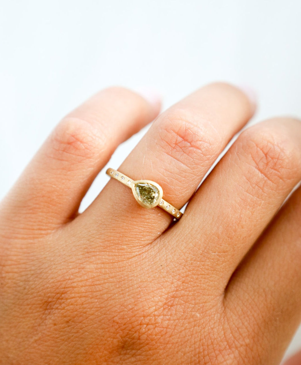 Gold ring with a green diamond on a person's finger against a white background