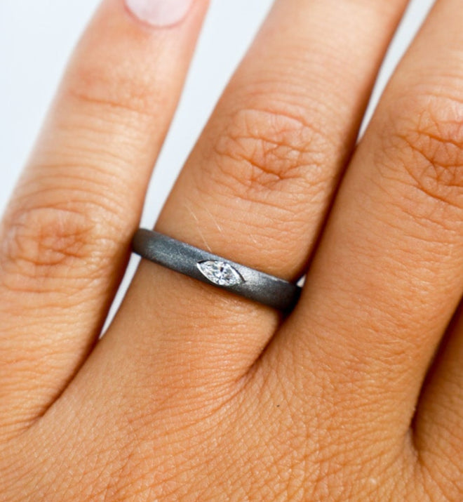 Close-up of a hand wearing a black gold ring with a small diamond on a light background