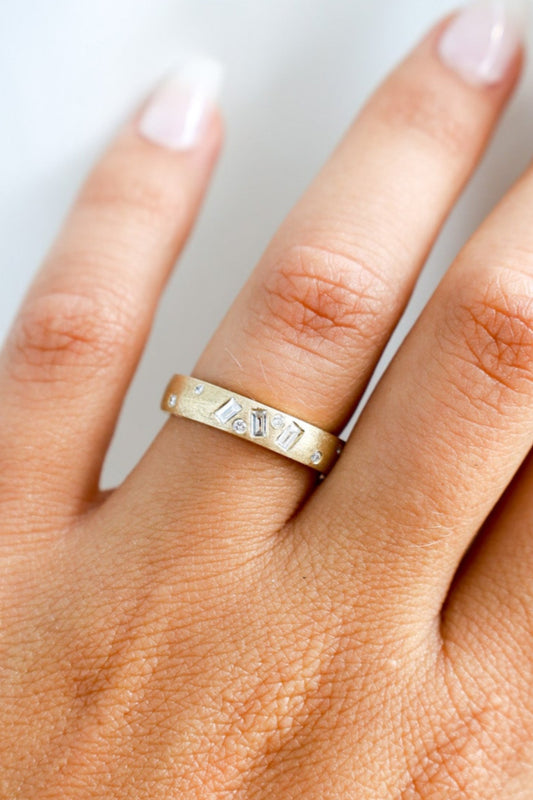 Gold ring with diamonds on a finger against a neutral background