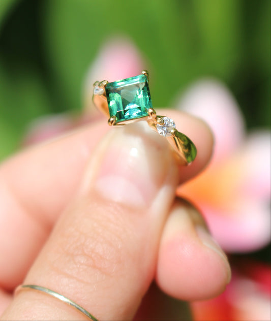 Green tourmaline ring with diamonds held between fingers with a blurred natural background
