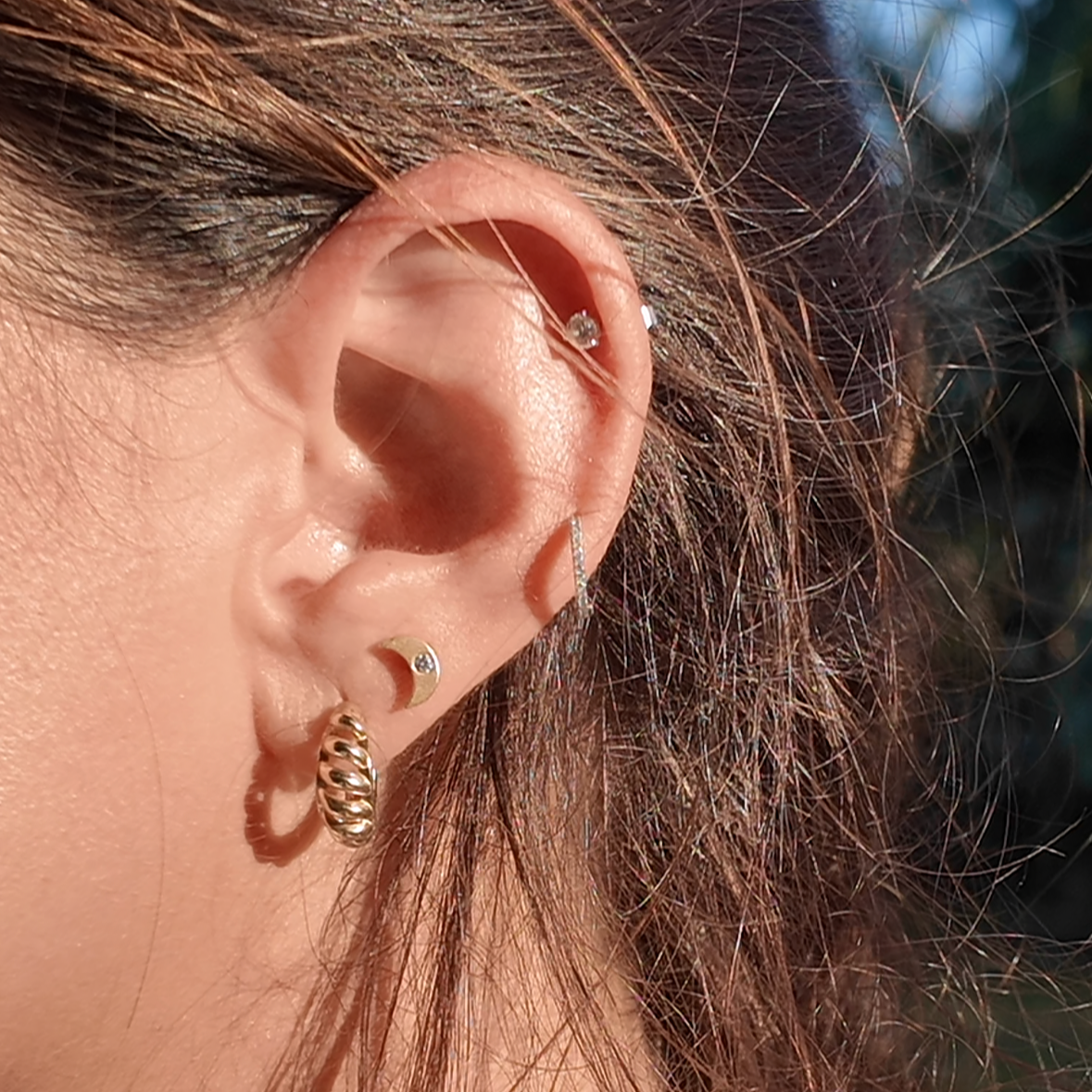 Close-up of an ear wearing gold earrings with a blurred natural background