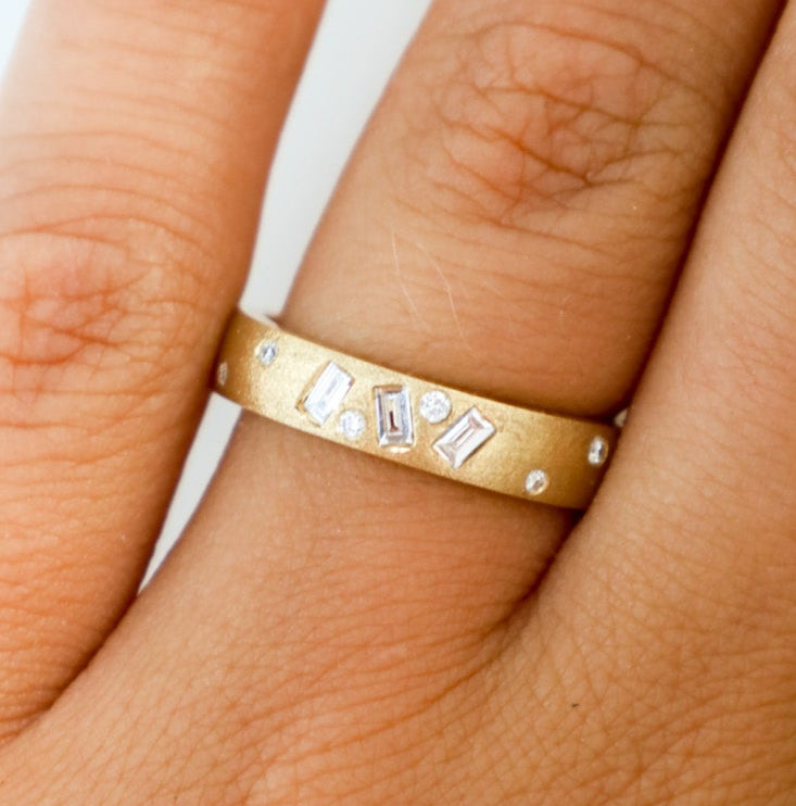 A gold vari-cut diamond ring with multiple shaped diamonds set around its circumference, worn on a finger.