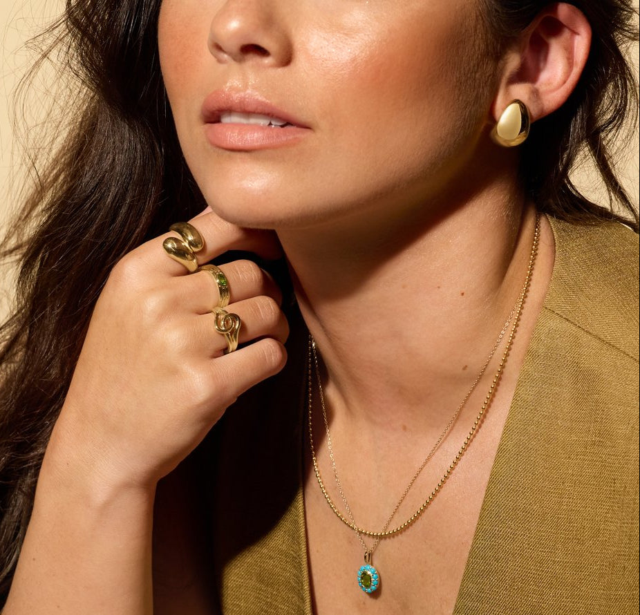 Woman wearing gold jewelry including earrings, rings, and a necklace.