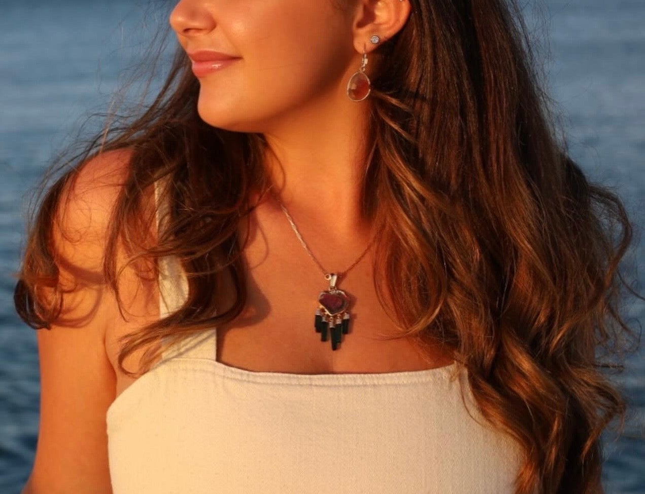 Woman with long hair and a necklace standing by a body of water