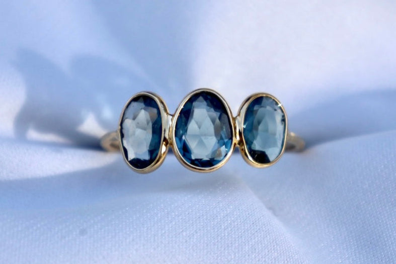 A ring with three London Blue Topaz drops set in a gold band, displayed on a white background.