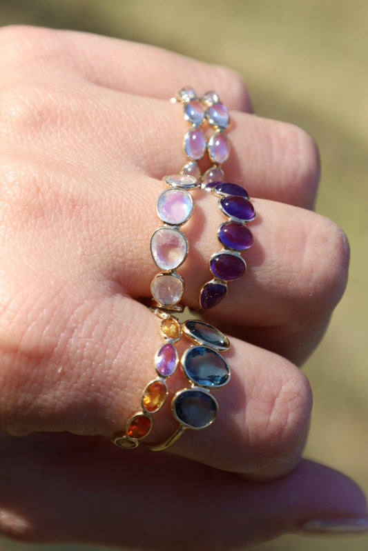 Hand wearing a colorful gemstone ring with a blurred natural background