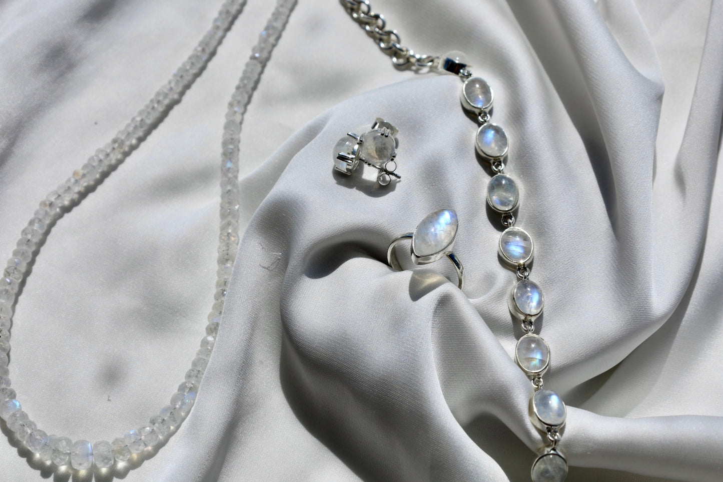 A sterling silver bracelet with alternating rainbow moonstones and clear crystals, displayed on a white fabric.