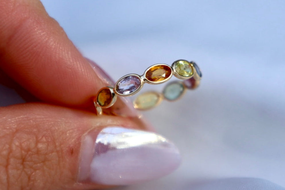 Close-up of a ring with multicolored gemstones held between fingers against a blurred background