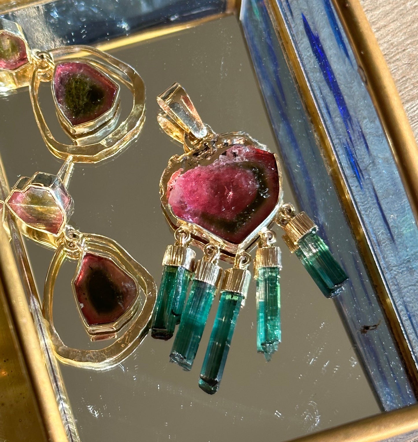Gold jewelry box with gemstone-encrusted earrings on a reflective surface