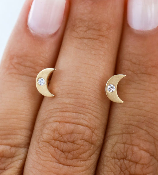 A hand wearing a brushed gold diamond crescent moon stud earring.
