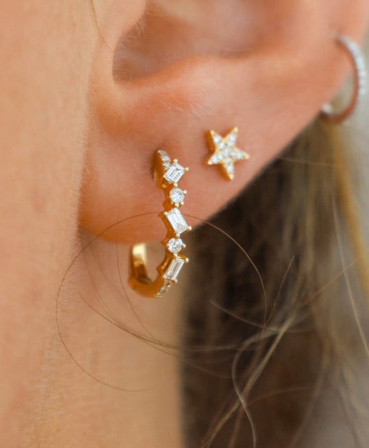 Close-up of an ear wearing gold hoop earrings with star details on a neutral background