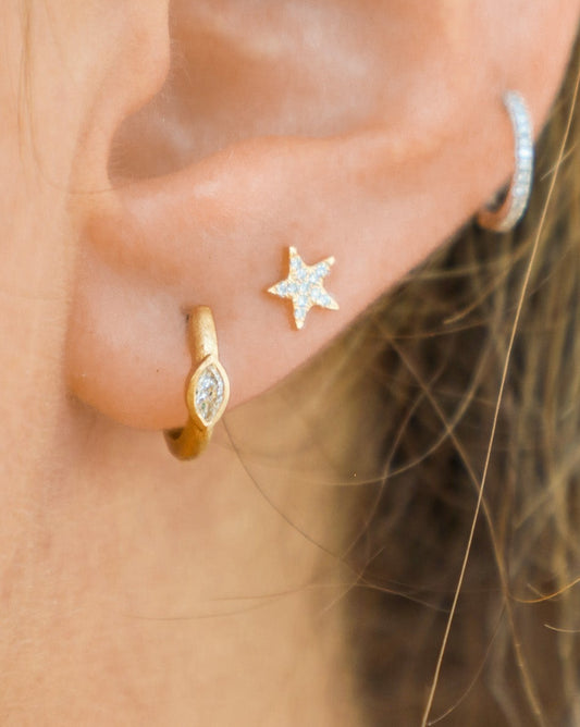 A close-up image of a person wearing a gold marquise diamond huggie earring in their left ear.