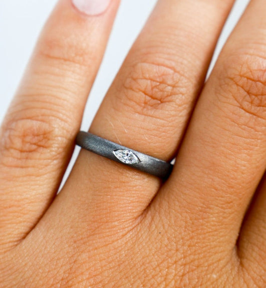 Close-up of a hand wearing a black gold ring with a small diamond on a light background