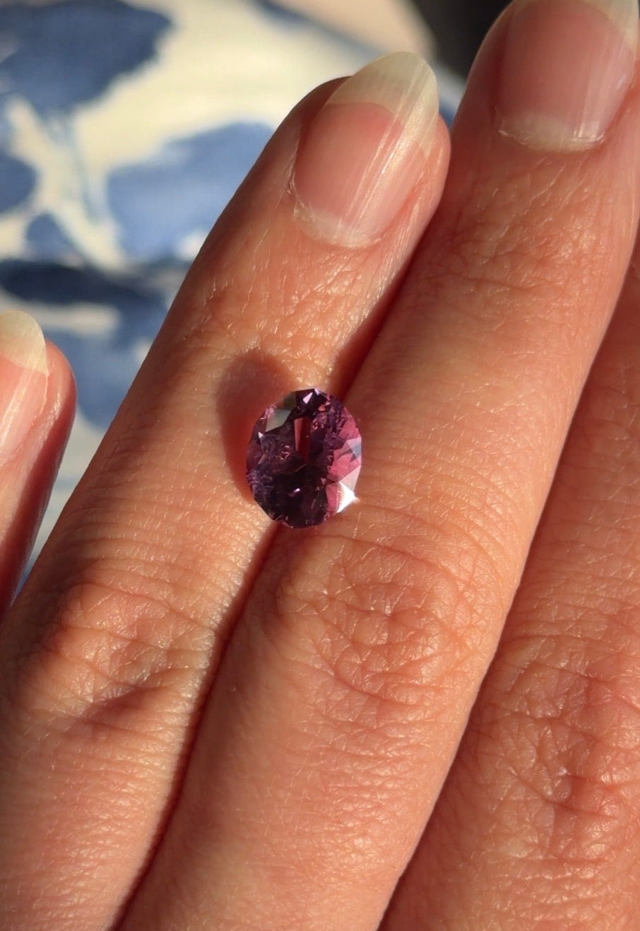 An oval shaped purple cuprian tourmaline displayed on a hand