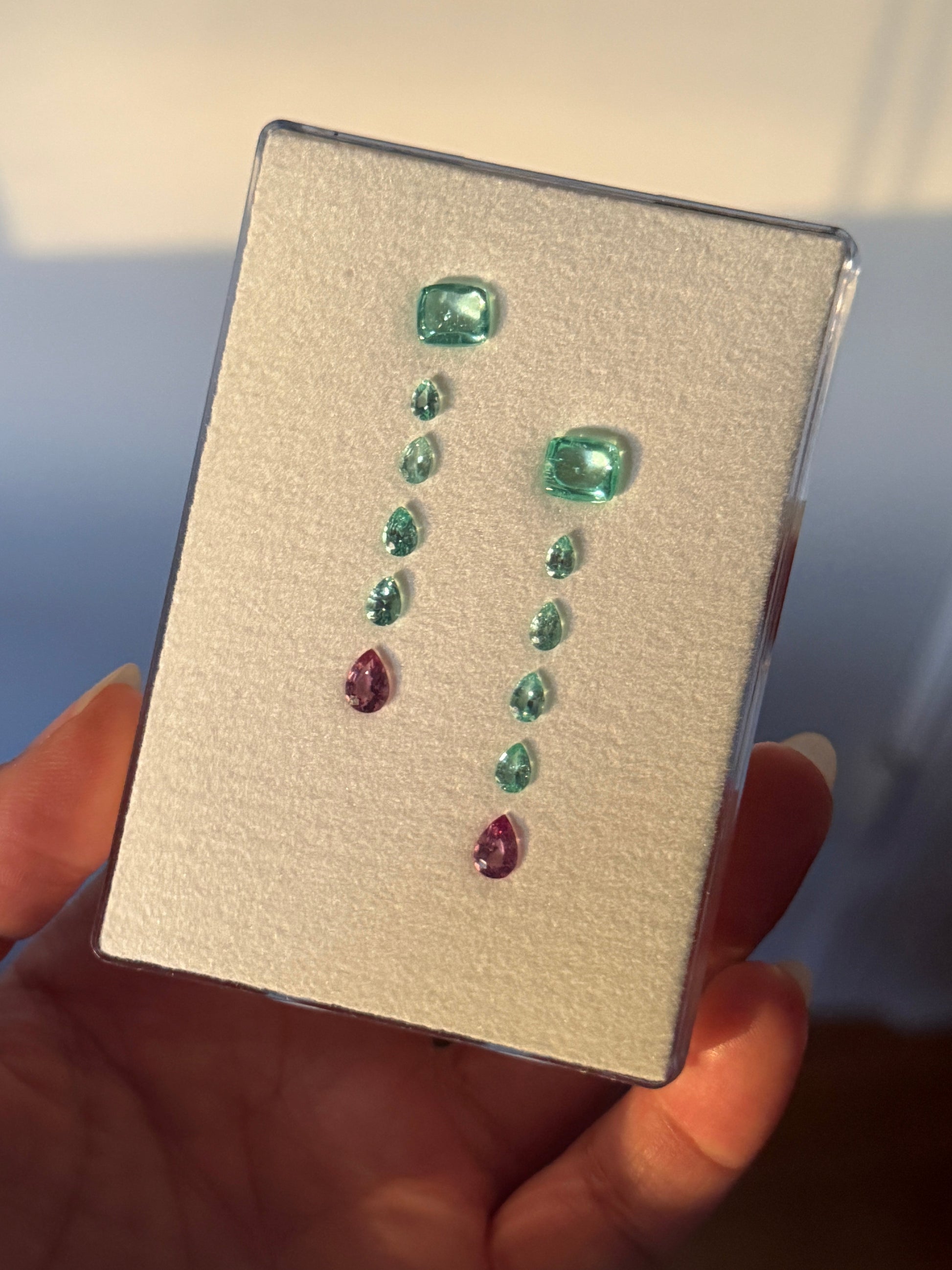 Collection of Paraíba tourmaline on a display card held by a hand.
