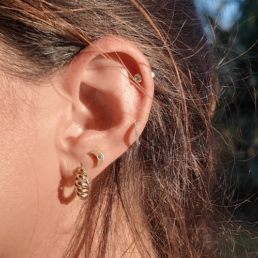 Close-up of an ear wearing gold earrings with a blurred natural background