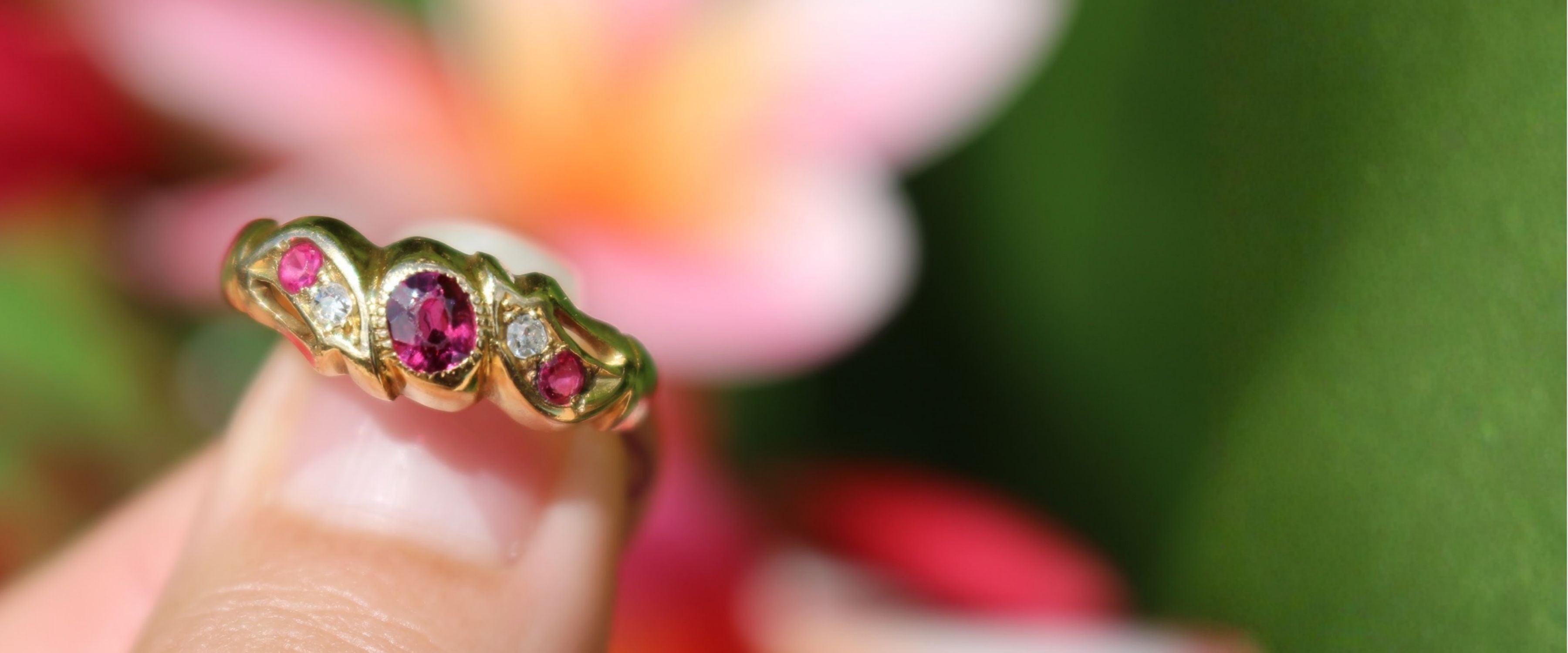 Gold ring with red gemstones on a blurred floral background