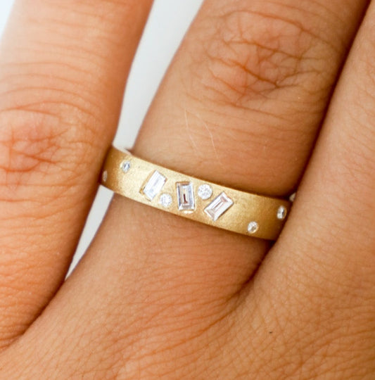 A gold vari-cut diamond ring with multiple shaped diamonds set around its circumference, worn on a finger.