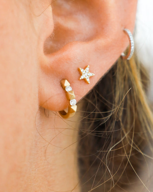 Close-up of an ear wearing gold hoop earrings with small diamonds and a star-shaped earring.