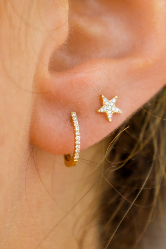 Close-up of an ear wearing a gold hoop earring and star-shaped stud earring.