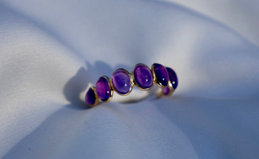 Gold ring with purple gemstones on a white fabric background