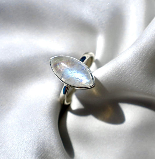 A silver marquise shaped moonstone ring on a white fabric surface.
