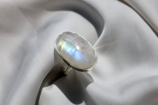 A silver-colored moonstone ring with a polished finish, displayed on a white fabric surface.