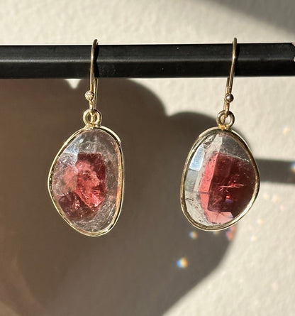 Teardrop-shaped earrings with pink gemstones held by a pencil against a white background