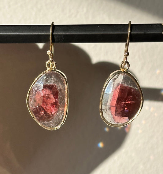 Teardrop-shaped earrings with pink gemstones held by a pencil against a white background